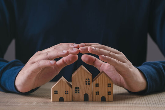 Hands protecting wooden house models symbolizing home insurance, property protection, real estate investment, mortgage security, family safety, financial planning, and residential risk management.