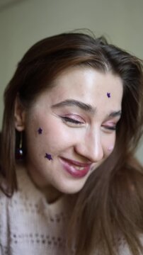 Vertical screen smiling young woman proudly shows colorful star shaped acne patches feeling more confident after accepting playful skincare as part of her beauty routine