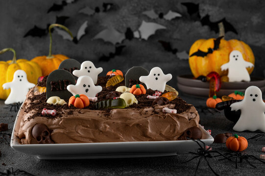 Halloween chocolate cake. Dirty cake with chocolate cream, decorated with worms, skulls, ghosts, pumpkins and sugar sprinkles on a dark background.