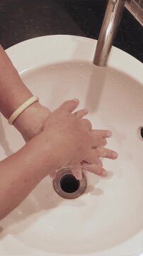 elderly asian woman scrubbing hands, properly washing her hand with liquid soap and tap water at sink, indoors scene, personal hygiene, healthy lifestyle and cleanliness concept, vertical video