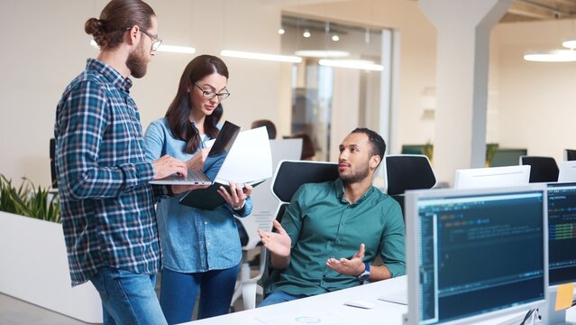 Team of young professional male and female IT specialists work in office and talking typing on laptop and computer indoors. Internet technologies. Modern tech company. Workflow in IT business
