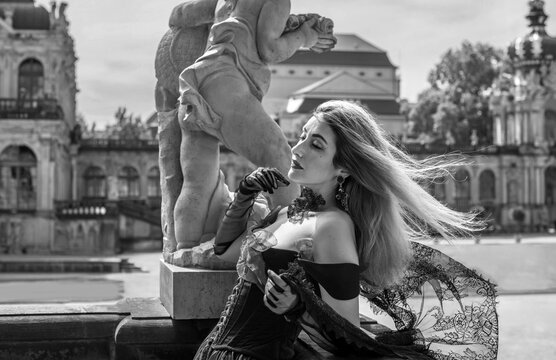 Woman in elegant deep red velvet corset top and black lace cape posing at a historic palace courtyard, fashion and premium lifestyle concept with modern vintage aesthetic