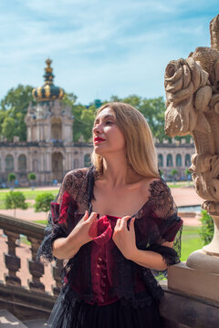 Woman in elegant deep red velvet corset top and black lace cape posing at a historic palace courtyard, fashion and premium lifestyle concept with modern vintage aesthetic