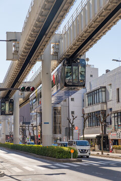 Chiba, Japan-February 1, 2026: Modern suspended monorail train traveling above a bustling city street on a bright sunny day with car and street traffic below.
