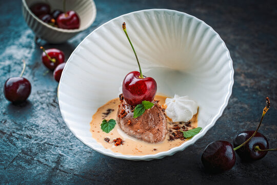 Modern dessert - dark black chocolate mousse au chocolat in vanilla sauce with black sweet cherries and meringues served as close-up in a design bowl