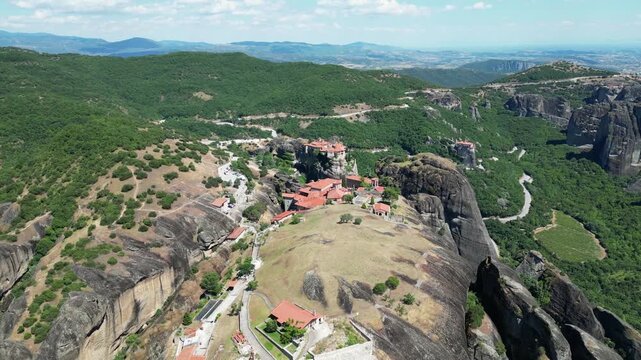 Aerial view of Holy Trinity monastery complex on massive rock formations surrounded by green hills in Meteora Kalabaka Thessaly Greece landscape stock video. High quality 4k footage