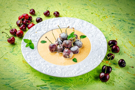 Deep fried sweet cherries dessert with vanilla sauce served as close-up in a design plate