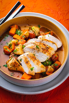 Braised chicken breast fillet with roasted vegetables pumpkin, pear and sweet potato in wine sauce served as close-up in a design bowl