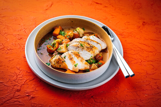Braised chicken breast fillet with roasted vegetables pumpkin, pear and sweet potato in wine sauce served as close-up in a design bowl