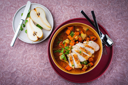 Braised chicken breast fillet with roasted vegetables pumpkin, pear and sweet potato in wine sauce served as top view in a design bowl