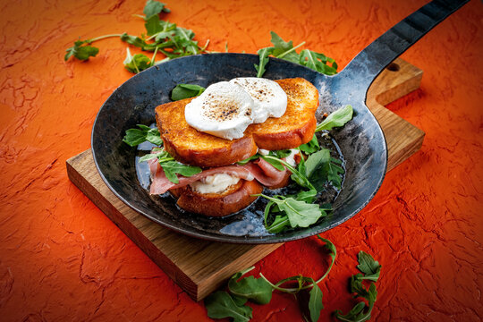 Traditional artisan croque monsieur chevre - hot brioche bread sandwich with prosciutto, arugula and goat cheese roasted in butter served as close-up in a rustic pan