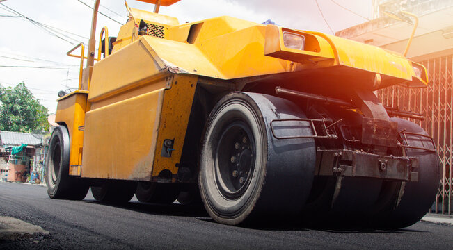 Yellow road roller compactor working on freshly paved asphalt, showing heavy construction machinery used for roadwork, pavement repair, street maintenance and infrastructure development.