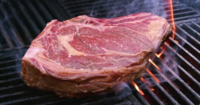 Barbecue dry aged entrecote roast beef steaks grilled as close-up on a charcoal grill with fire and smoke - outdoor video