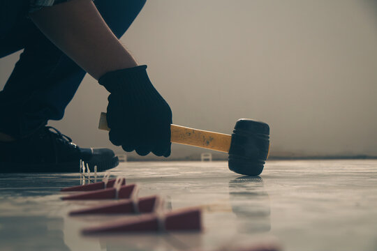 The craftsman is using a hammer to break tiles and level the surface.