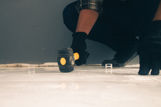 The craftsman is using a hammer to break tiles and level the surface.