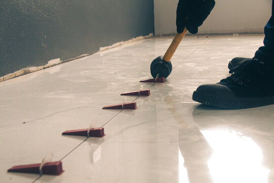 The craftsman uses a hammer to break the leveling lock and then hammers the tiles.