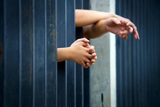 Child&rsquo;s Hands Clutching Prison Cell Bars with Outstretched Hands Behind Fence