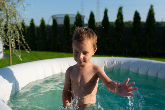 Toddler boy splashing water in backyard inflatable pool