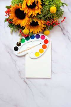watercolor palette with brush, empty paper sheet and autumnal bouquet with sunflowers on marble table background. Desk of creative worker, Painter workplace. symbol of Arts. top view. copy space