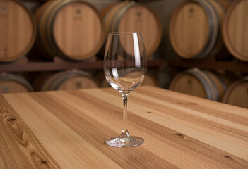 Naklejka premium Wine tasting and winemaking process, empty wine glass on a wooden table in a cellar with oak barrels