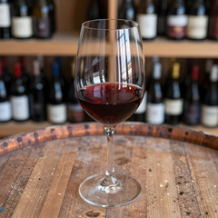 Naklejka premium Red wine tasting experience, glass of merlot on a rustic wooden barrel in a winery cellar with bottles