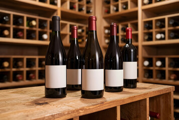 Naklejka premium Wine cellar and tasting experience, red wine bottles with blank labels on a rustic wooden table, luxury beverage storage