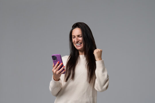 Excited adult woman celebrating success looking at smartphone screen holding fist up