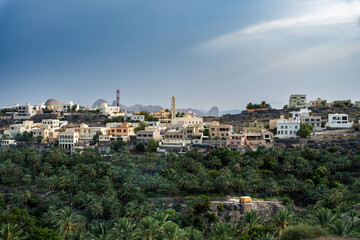Fototapeta premium Traditional mountain settlement surrounded by lush palms and dramatic mountains in Oman