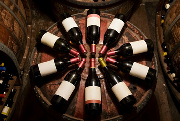 Naklejka premium Wine tasting and cellar storage, red wine bottles arranged on a wooden barrel in a dark winery