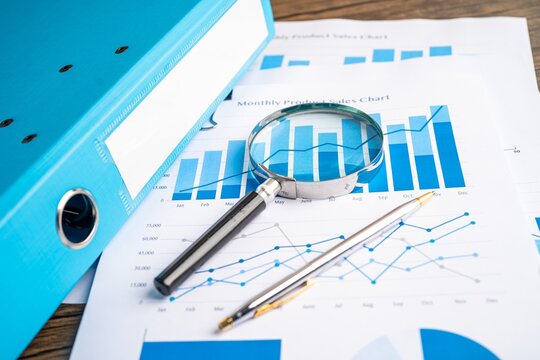 Financial charts and analytics reports with magnifying glass and blue folder on wooden office desk, analytics