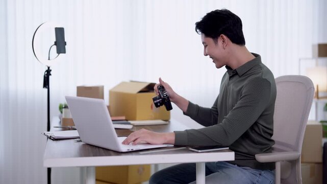 Young Asian online seller checking digital camera while managing laptop for live streaming ecommerce business at home office with copy space