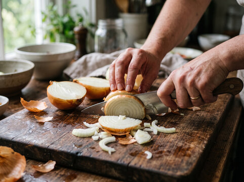 A person skillfully chopping an onion on a wooden cutting board in a kitchen