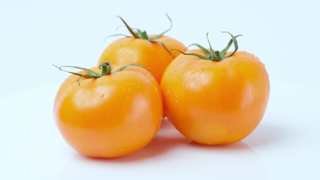 Group of three ripe yellow orange tomatoes with water droplets rotating on a white background. Fresh organic vegetables studio shot close up.	
