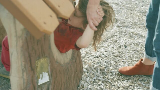 Boy climbing and playing on wooden playground structures with mother nearby