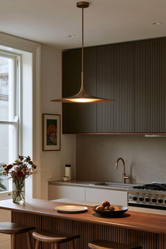 Slim brushed brass pendant lamp illuminating walnut breakfast bar in a Mid-Century Modern kitchen with soft morning light from the window