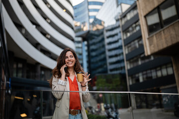 Obraz premium Professional woman talking on smartphone drinking coffee in city