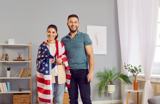 Happy smiling American people standing close at home, woman wearing USA national flag on her shoulders. Patriotic smiling couple, celebrating sate holiday, American Patriot Day, feeling country pride