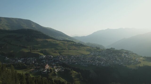 Aerial footage of scenic mountains and green forests under a cloudless blue sky during summer.