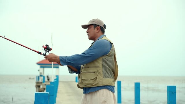 Happy senior man sitting by the sea and fishing with a rod after retirement. Active aging, healthy longevity, outdoor leisure, fulfilling retirement. Life insurance and financial security concept.
