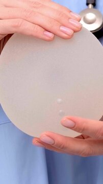 A doctor holding a silicone breast implant sideways, showing profile shape and contour, plastic surgery consulting, implant shape, anatomical design.