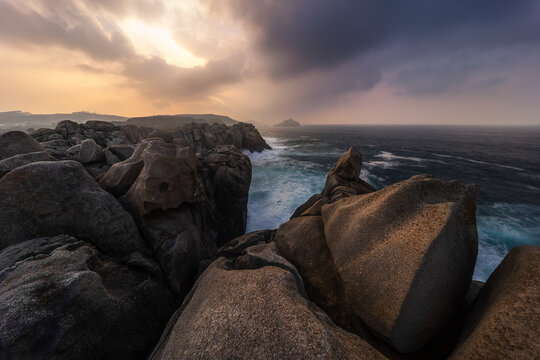 View of the dramatic rock formations at Cantis de Papel with crashing waves and golden hour light over the Atlantic Ocean in Moras, Lugo, Spain.
