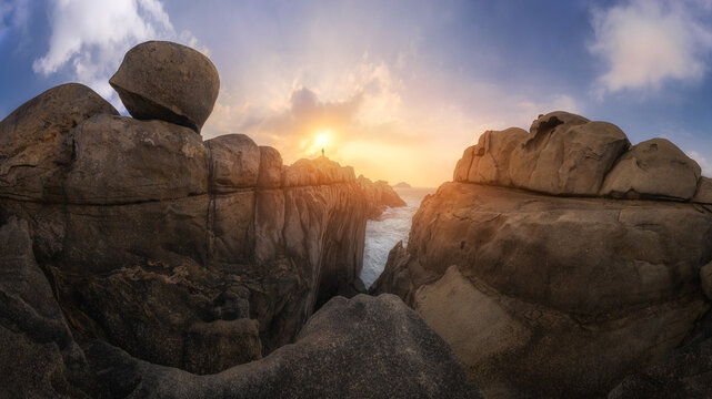 View of the dramatic rock formations of Cantis de Papel at sunset, with a person standing on the cliff edge overlooking the ocean in Moras, Lugo, Spain.