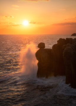 View of the Cantis de Papel rock formation with waves crashing against the cliffs during a vibrant golden hour sunset in Moras, Lugo, Spain.