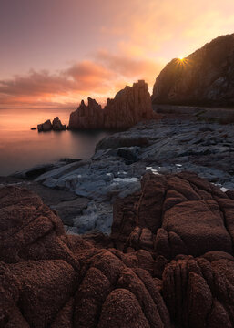 View of the iconic red granite rock formations of Rocce Rosse at sunrise, with calm sea and rugged coastal landscape in Arbatax, Sardinia, Italy.