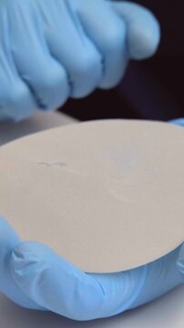 Doctor in blue medical gloves holding a round breast implant during a consultation in a clinic, healthcare advertising, plastic surgery, aesthetic medicine, mammoplasty procedure.
