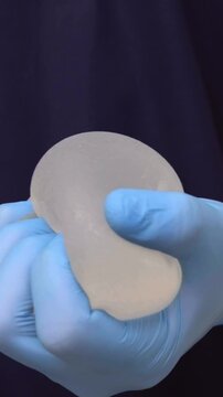 Specialist in blue gloves demonstrating flexibility of a silicone breast implant in a clinic, medical presentation, aesthetic surgery, reconstructive medicine, plastic surgery.