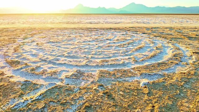 Tire tracks forming circular patterns on white salt crust beneath glowing golden sunset skies in Utah