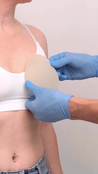 A doctor in blue gloves adjusts a breast implant next to a woman patient during a medical consultation in a clinic, aesthetic medicine, plastic surgery planning, patient examination.