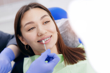 Young asian female receiving dental brace adjustment at clinic, choosing dental veneer shade