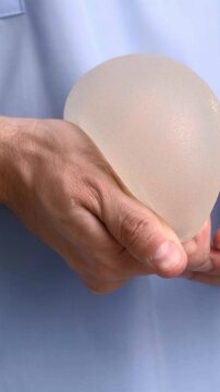 A medical specialist demonstrating a breast implant shape and firmness during a patient consultation in a plastic surgery clinic, healthcare and aesthetic medicine, clinical education.